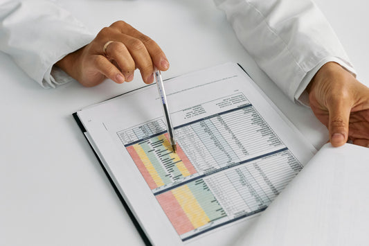 A clipboard with papers that contain a table of data and hands holding the paper and a pen.