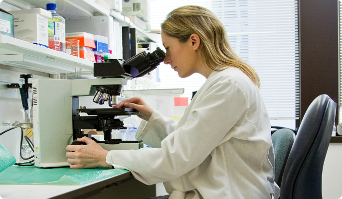 Scientist looking through a microscope in a medical setting. 