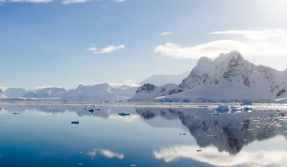 Snowy mountain range reflected in calm water under a blue sky.
