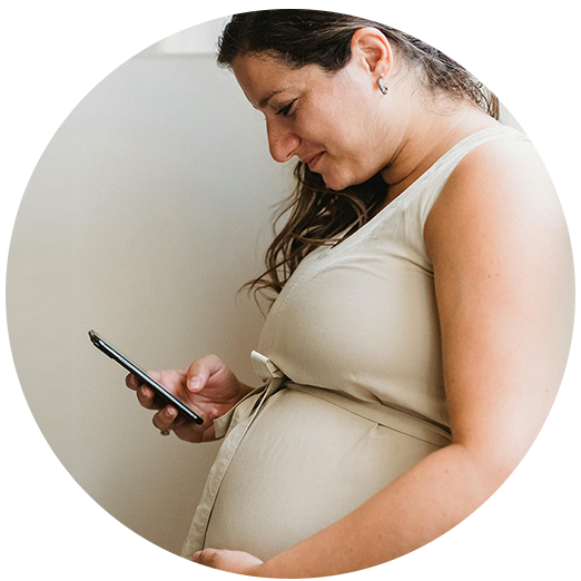 Side profile image of a heavily pregnant lady looking down at her phone in her hand. 