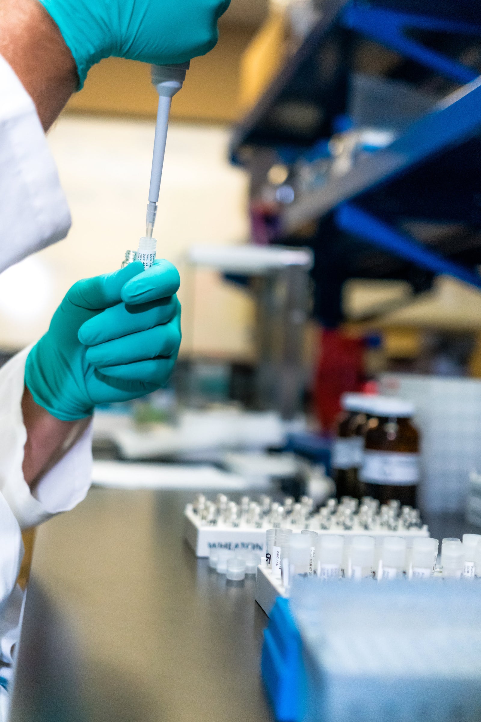Laboratory setting with gloved hands using a pipette on a lab bench.