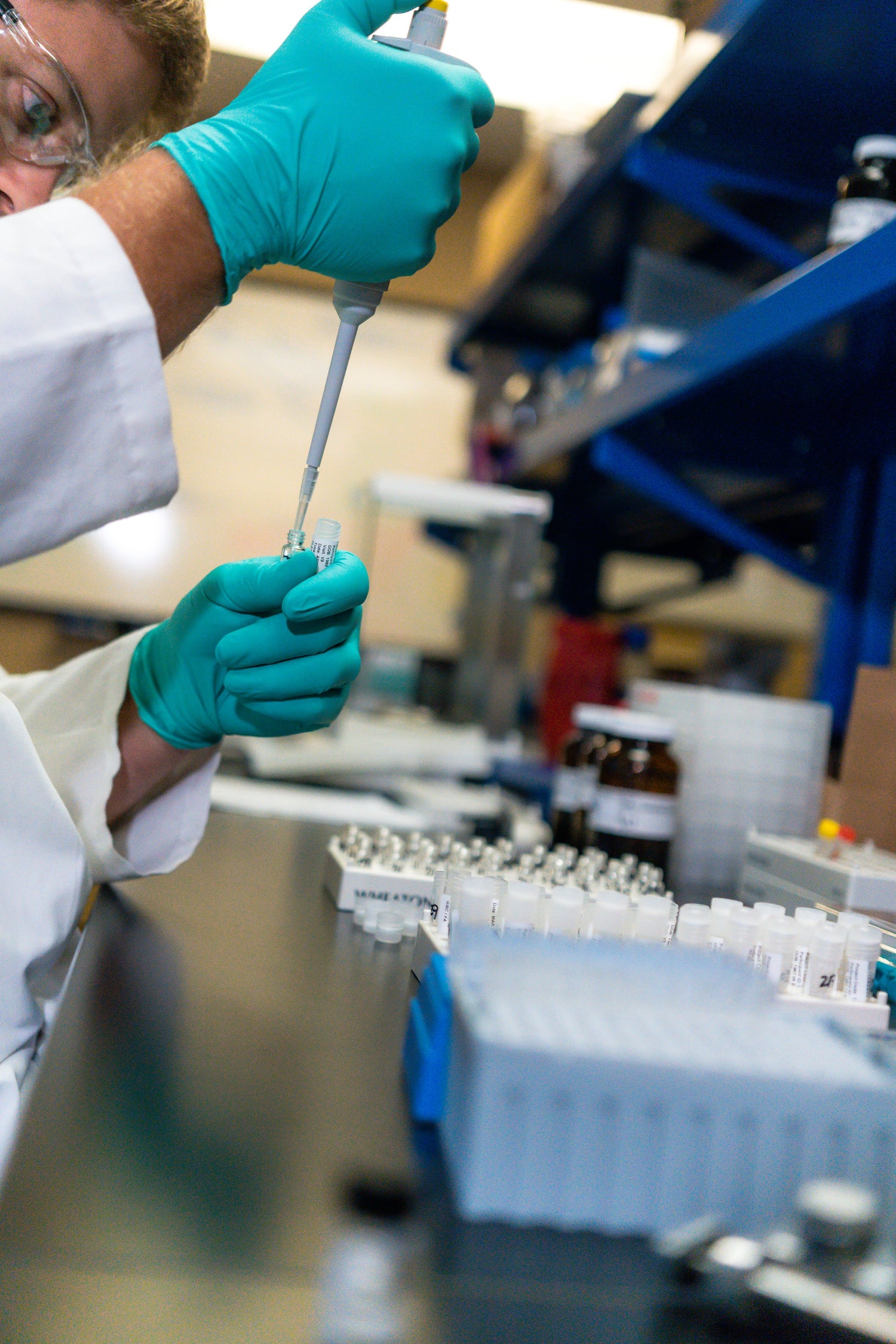 Person in lab coat and gloves using a pipette in a laboratory setting.