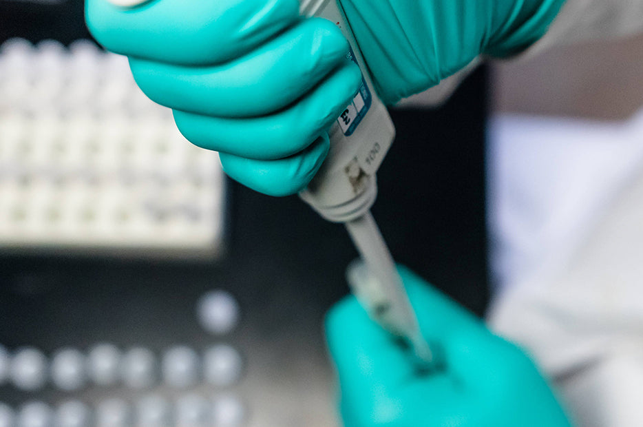 Person in green gloves using a pipette in a laboratory setting.