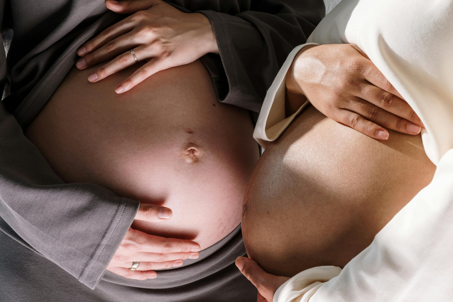 A close up of two pregnant bellies being cradled next to each. 