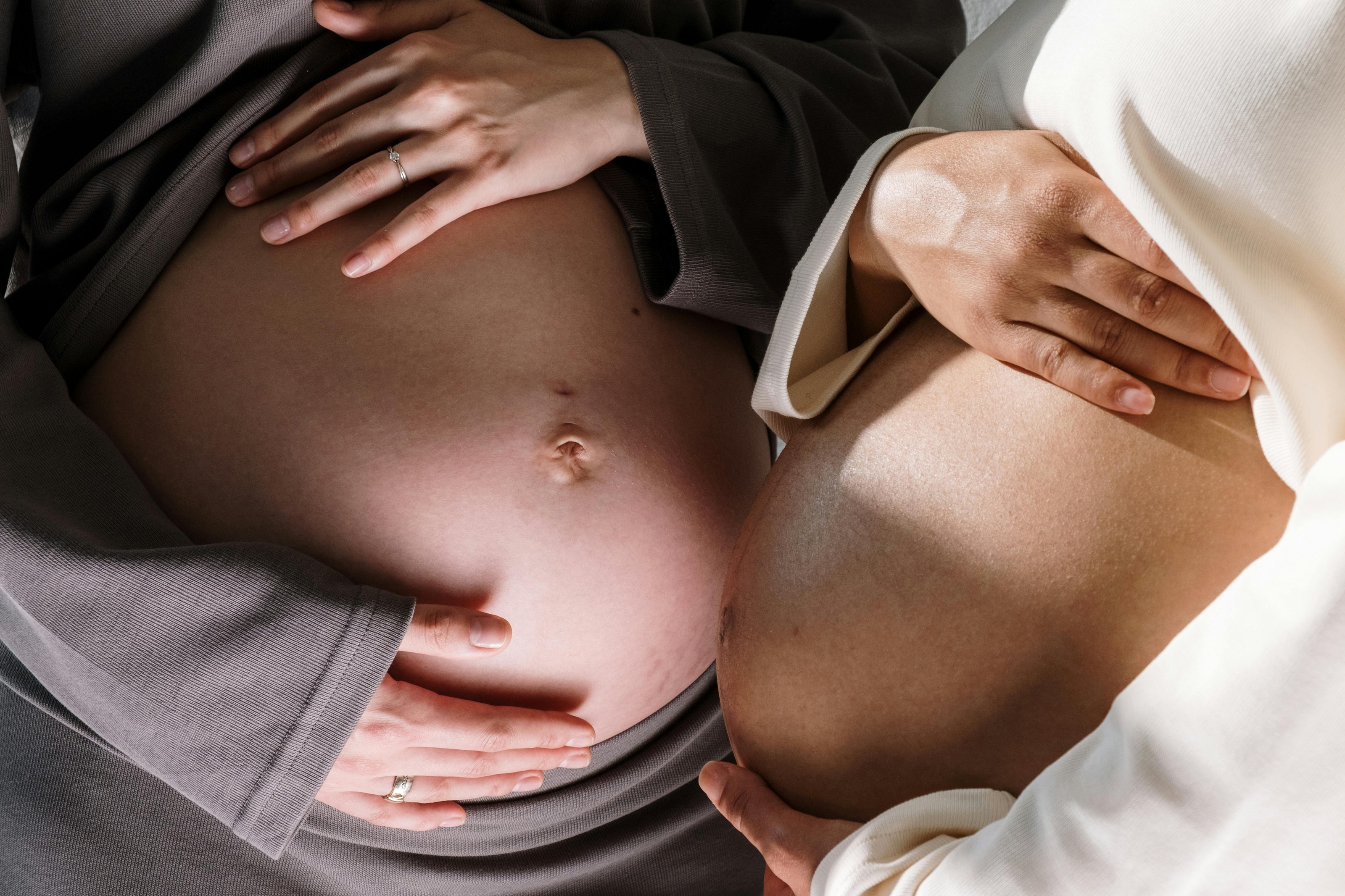 A close up of two pregnant bellies being cradled next to each. 
